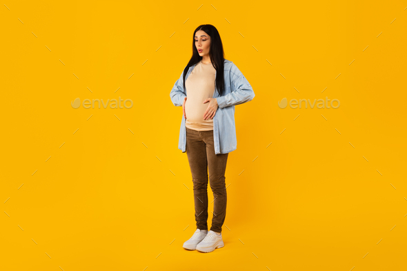 Full body length shot of pregnant woman suffering from abdomen pain, touching belly and breathing