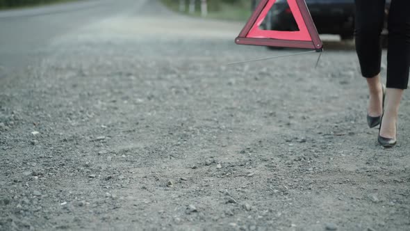 Unrecognizable Woman with Broken Automobile Installing Red Triangle Sign on Road alt