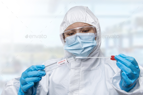 NHS technician holding COVID-19 swab collection kit wearing white PPE protective suit and mask