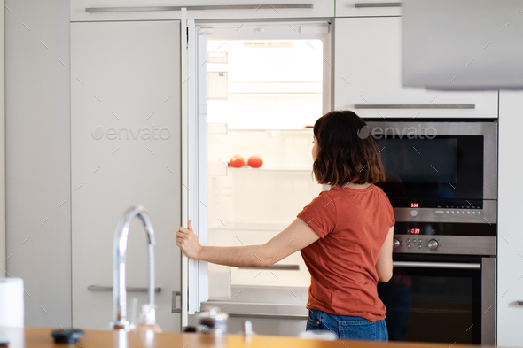 Young Housewife Searching For Food In Empty Fridge In Kitchen