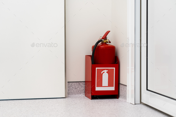 Red fire extinguisher stands in the corner of the room. Life safety concept.