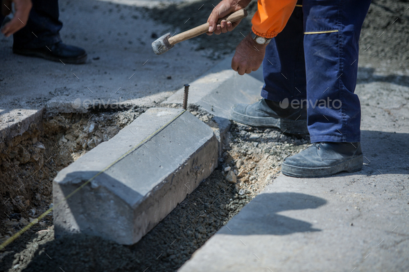 Worker with an orange uniform installing a sidewalk with a big hammer