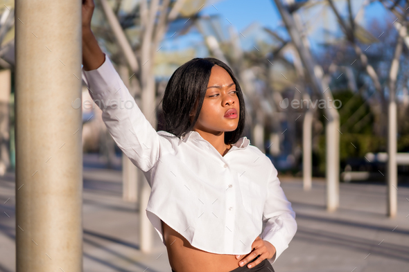 Young african woman in white clothes in the city sunset doing a fashion posing looking to the right