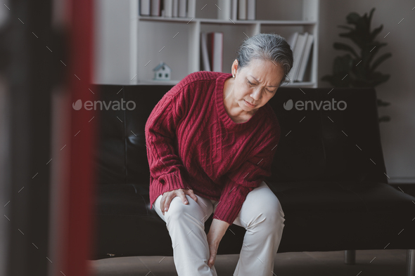 Senior woman sitting in the living room at home and showing body aches, aging sickness, body aches o