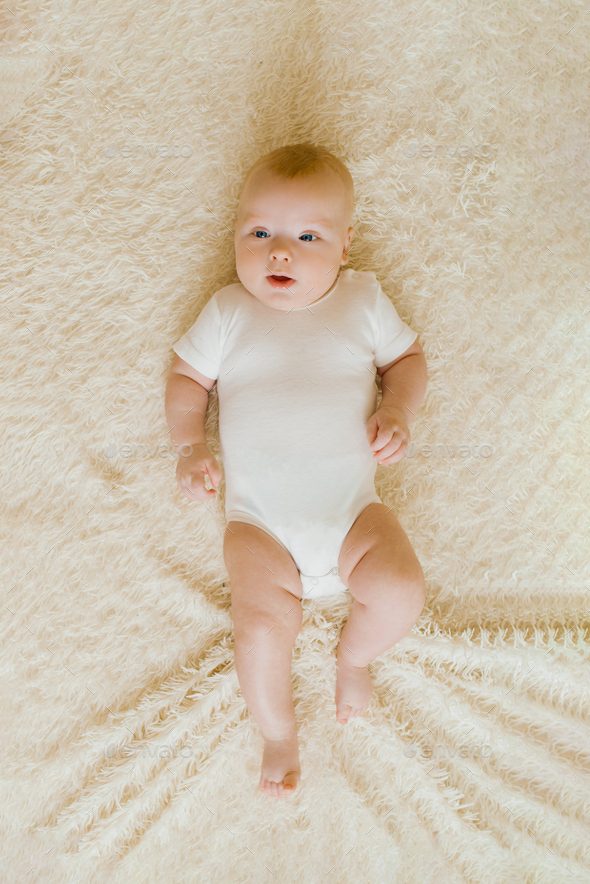 Fivemonthold baby is lying on a light blanket in the bedroom. Top