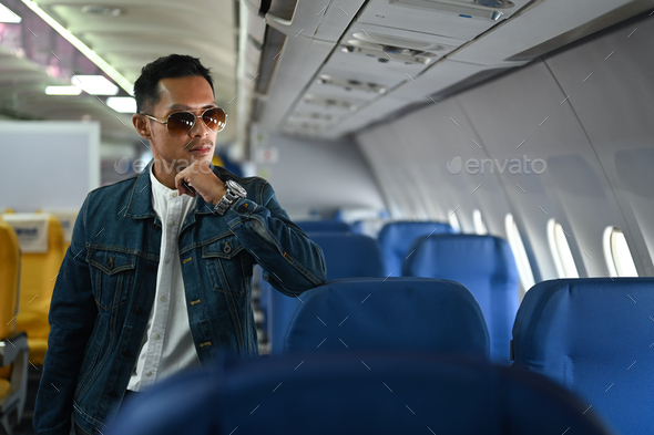 Portrait of hipster man traveller in sunglasses and jean jacket leaning on the airline seats.
