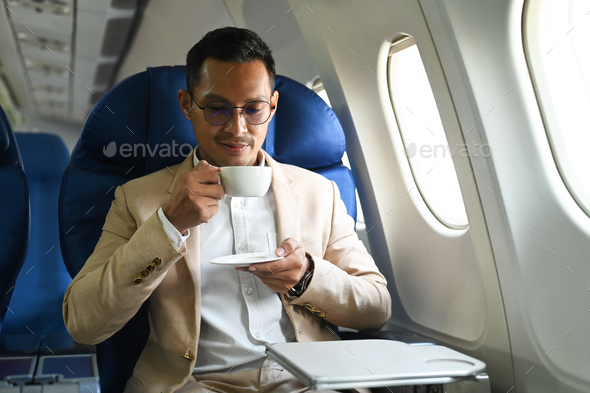Businessman drinking coffee, relaxing in comfortable seat next to aircraft cabin window.