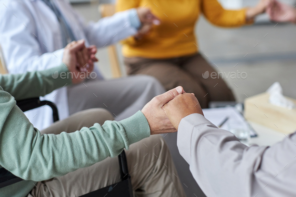 Close up of elderly people holding hands in circle during support group session