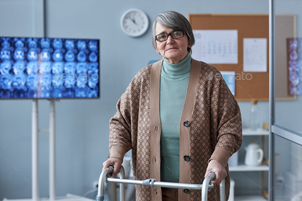 Waist up grey haired senior woman using mobility walker in medical clinic