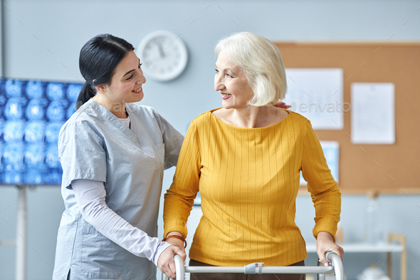 Waist up smiling young nurse helping senior woman using mobility walker