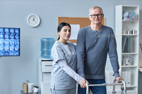 Nurse and senior patient looking at camera in clinic using mobility walker