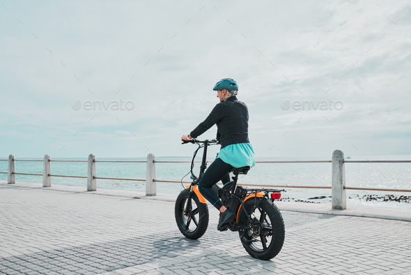 Mature woman, helmet or electrical bike by beach for future fitness, clean energy transport or sust