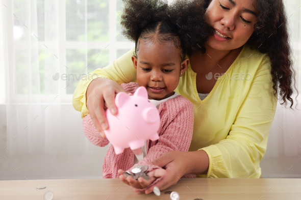 Daughter and happy mother saving money putting coin of cash into piggy bank