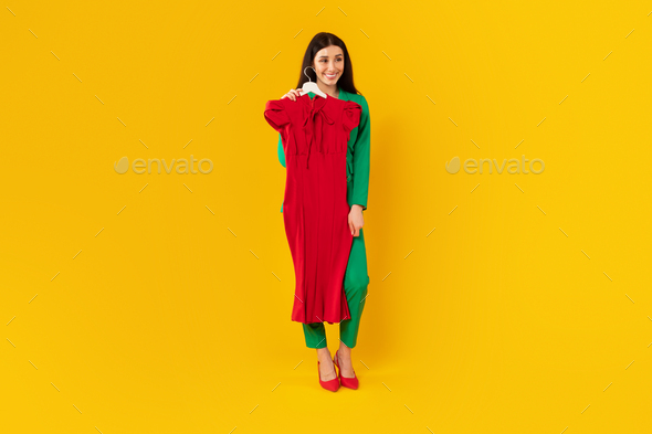 Full length shot of fashion designer woman standing with hanger in hand fitting on red elegant dress - Stock Photo - Images