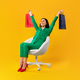 Full body length shot of contented shopaholic woman sitting on chair and raising hands with shopping - PhotoDune Item for Sale