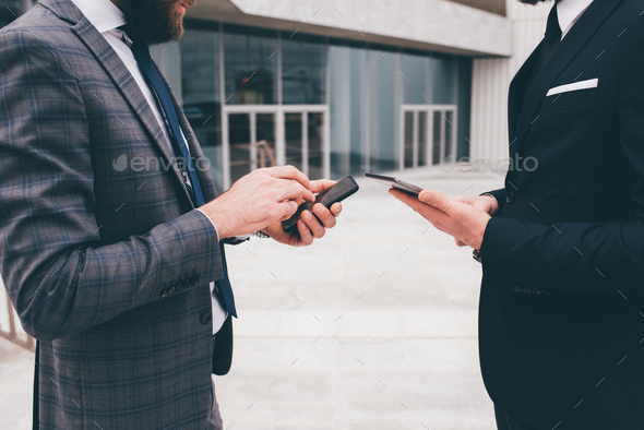 Two unrecognizable young elegant businessman outdoors using smartphone - Stock Photo - Images