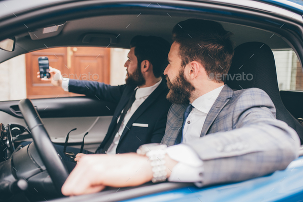 Two elegant contemporary bearded businessmen taking selfie seated in car - Stock Photo - Images