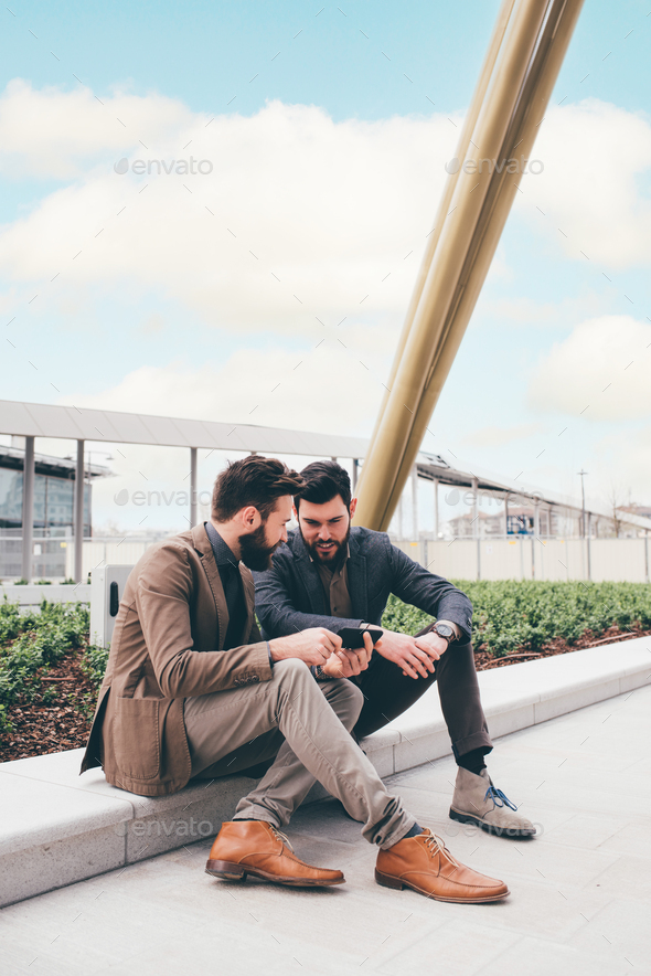 Two young businessman sitting outdoors sharing and using tablet - Stock Photo - Images