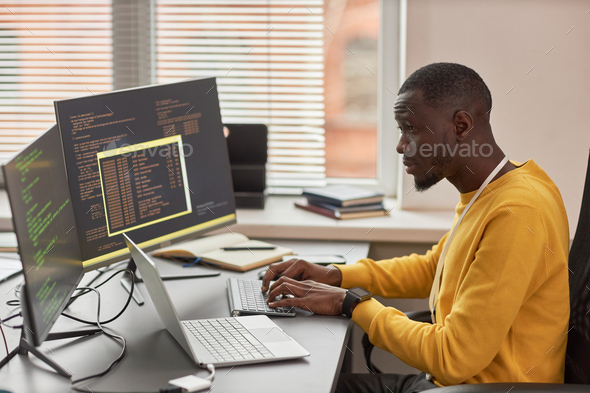 Young black man typing at keyboard and writing code in IT development company