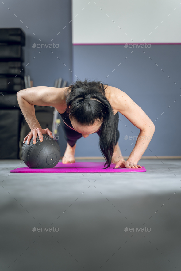 Vertical shot of an Asian woman performing arm push-ups, with one hand over a weight ball.
