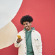 Happy young African American guy standing at color wall using mobile phone. - PhotoDune Item for Sale