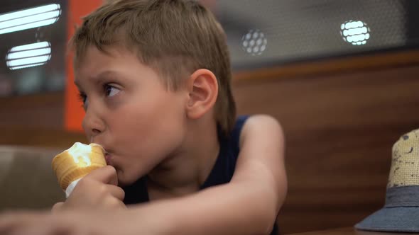 Adorable Little Caucasian Boy Eating Icecream Cone at the Table in Cafe