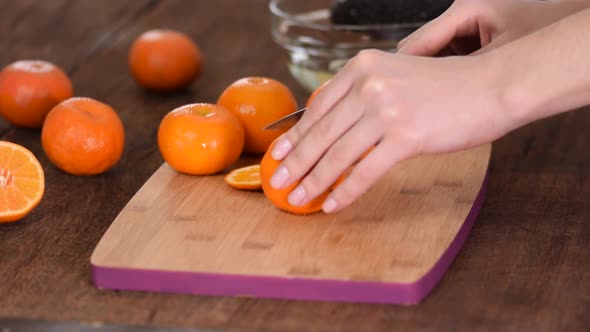 A Closeup of Female Hands Cutting a Fresh Tangerine on a Cutting Board
