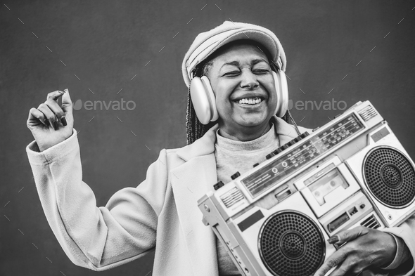 Happy african senior woman listening music in boombox vintage stereo