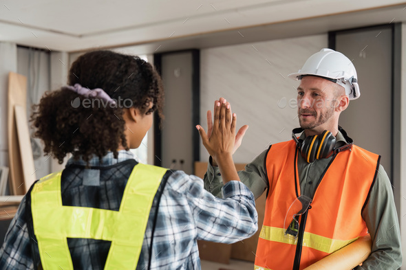 Construction engineer with blueprint making high five while standing on construction site. Home - Stock Photo - Images