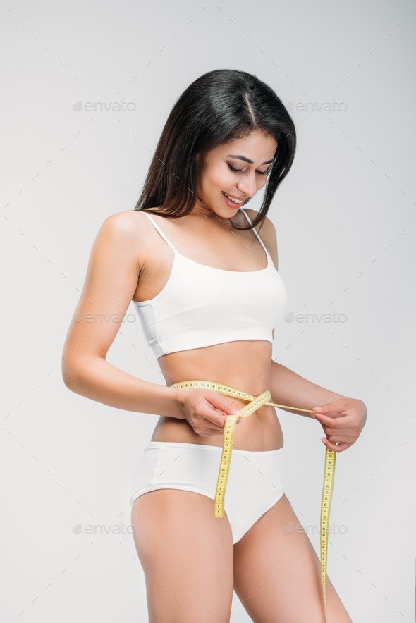 smiling african american girl in underwear measuring her waistline,  isolated on grey Stock Photo by LightFieldStudios