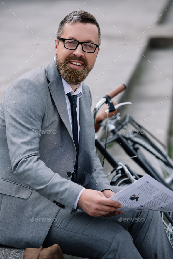 handsome bearded businessman with newspaper sitting on stairs with bicycle