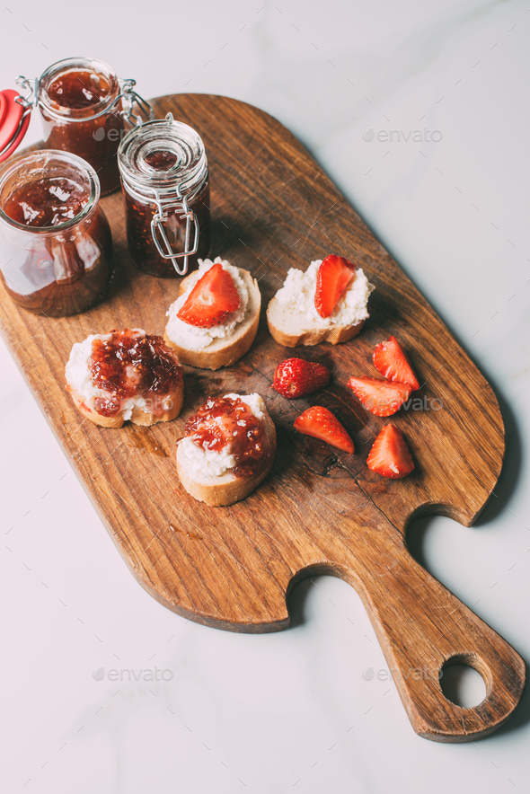top view of cutting board with fruit jam in jars and sandwiches with
