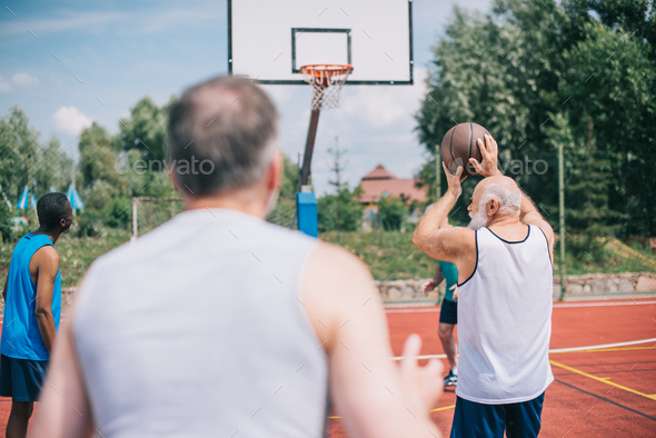 selective focus of interracial elderly sportsmen playing basketball together on playground