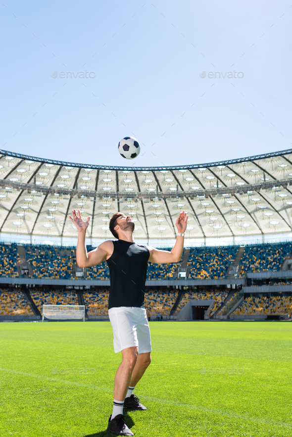 sportive young soccer player bouncing ball on head at sports stadium Stock Photo by
