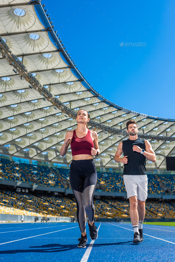 Fit Young Male And Female Joggers Running On Track At Sports Stadium