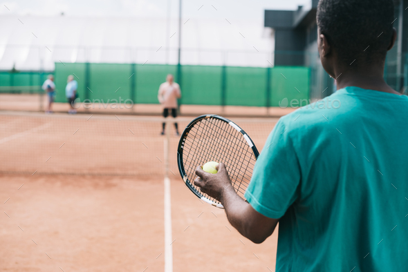 selective focus of elderly african american man playing tennis with friend on court