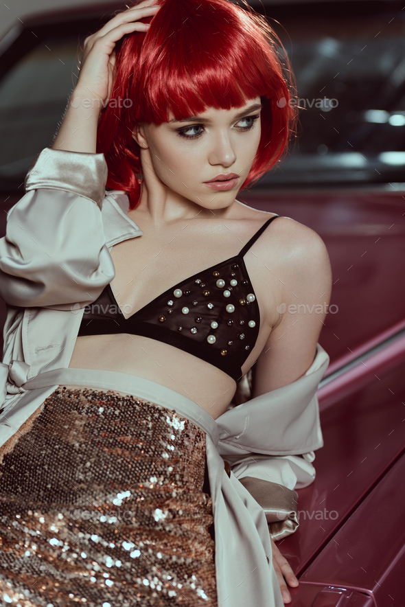 beautiful young woman in red wig and bra leaning at car and