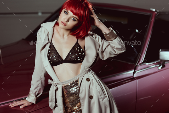beautiful girl in red wig, bra and trench coat looking at camera