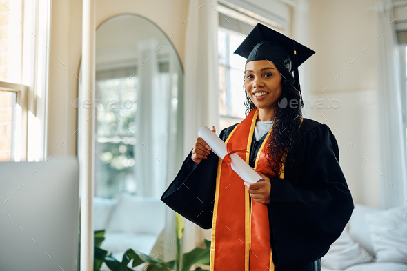 Happy black student in graduation gown holding her master\'s degree and looking at camera.