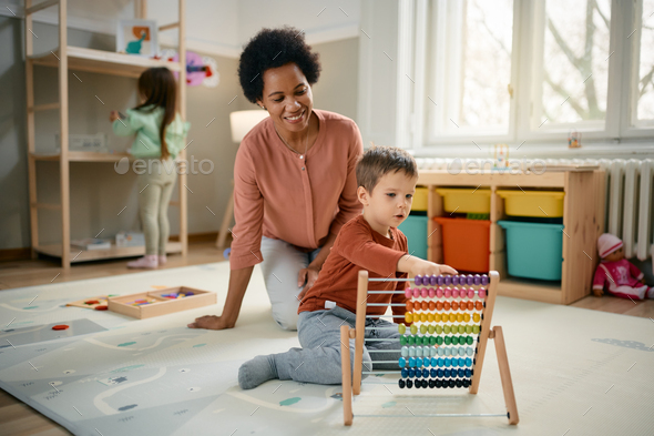 Little boy using abacus while learning to count with teacher's assistance at kindergarten.