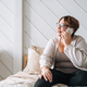 Smiling middle aged plus size woman using mobile phone on bed at home - PhotoDune Item for Sale