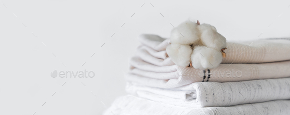 Cotton branch with pile of folded bed sheets and blankets.Organic lifestyle and skin care products