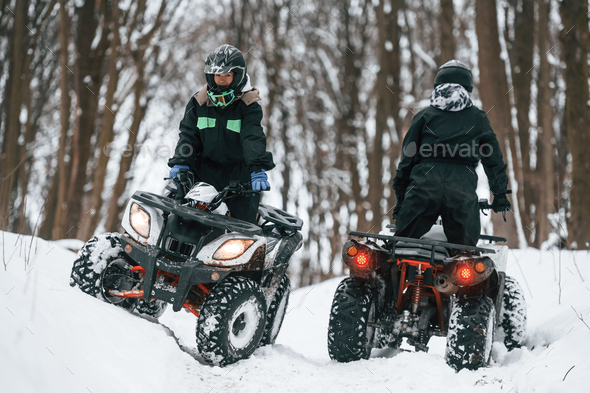 Riding the opposite ways. Two people are on the ATV in the winter forest