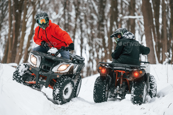 Riding the opposite ways. Two people are on the ATV in the winter forest