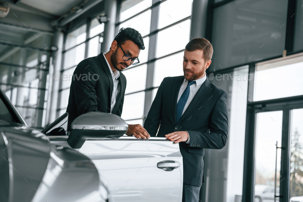 Business partners. Man is consulting the customer in the car showroom