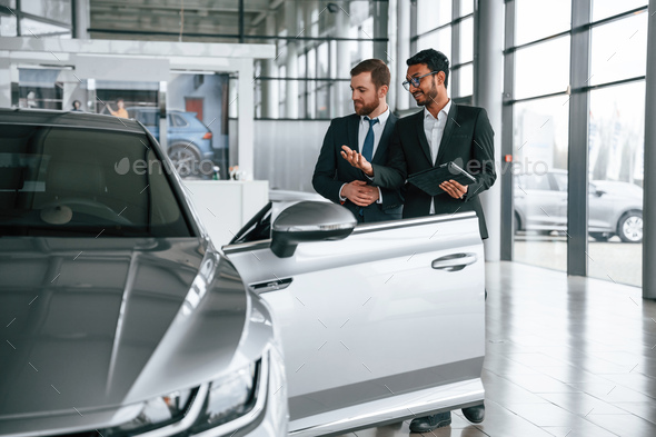 Business partners. Man is consulting the customer in the car showroom