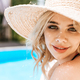 portrait of beautiful young blonde woman in straw hat smiling at camera near pool - PhotoDune Item for Sale