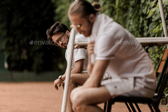 side view of retro styled tennis players sitting on chairs at tennis court