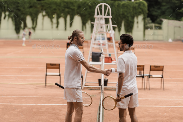 side view of retro styled tennis players shaking hands above tennis net at court