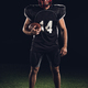 confident american football player holding ball in hand and looking at camera isolated on black - PhotoDune Item for Sale